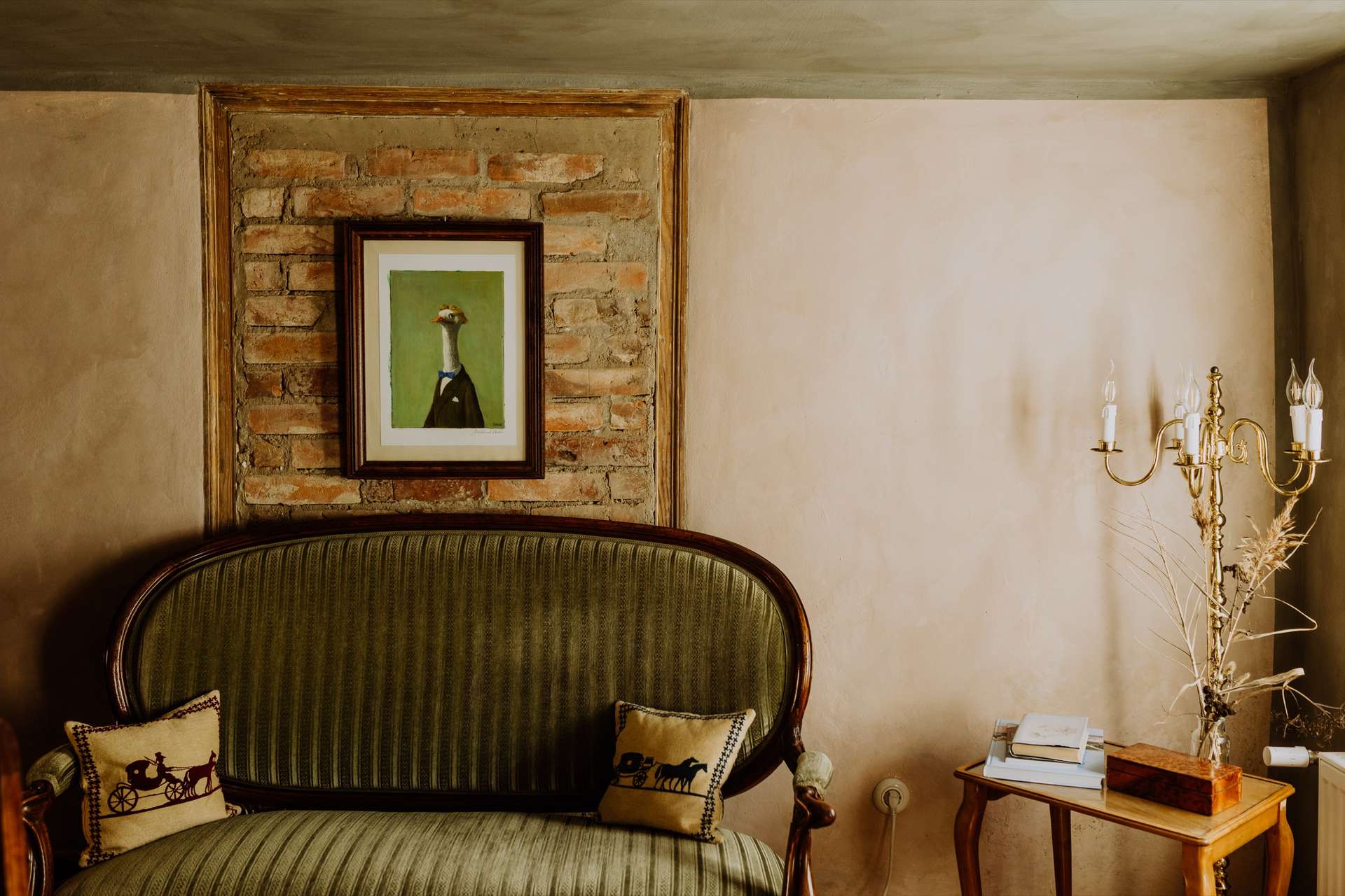 Biedermeier-Lounge mit grün gestreiftem Sofa, freigelegter Ziegelnische und Messing-Kandelaber