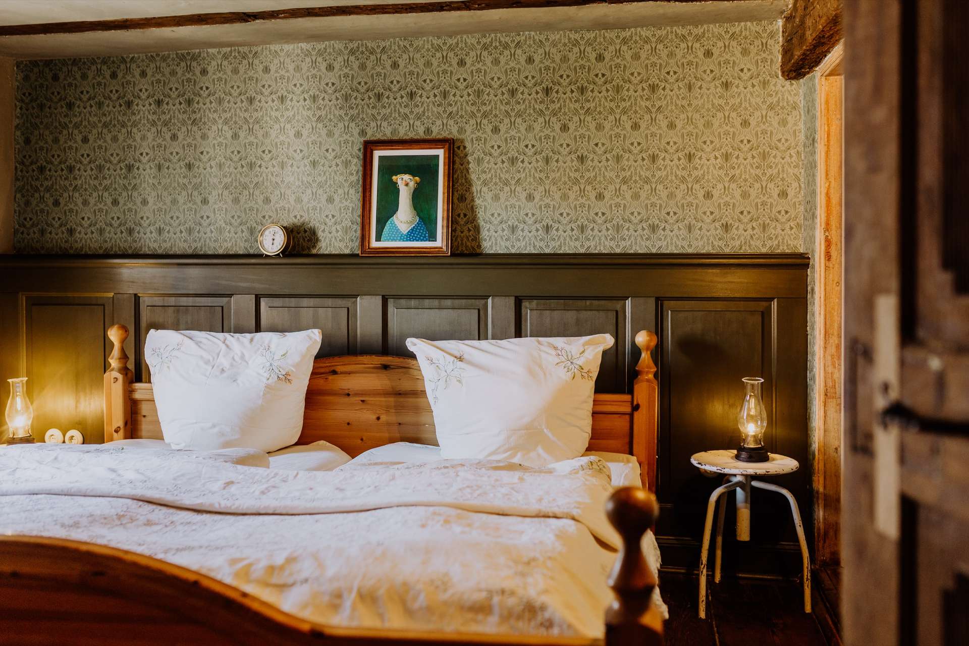 Schlafzimmer mit Doppelbett, weißer Leinenwäsche, dunkelgrüner Kassettenvertäfelung und botanischer Tapete