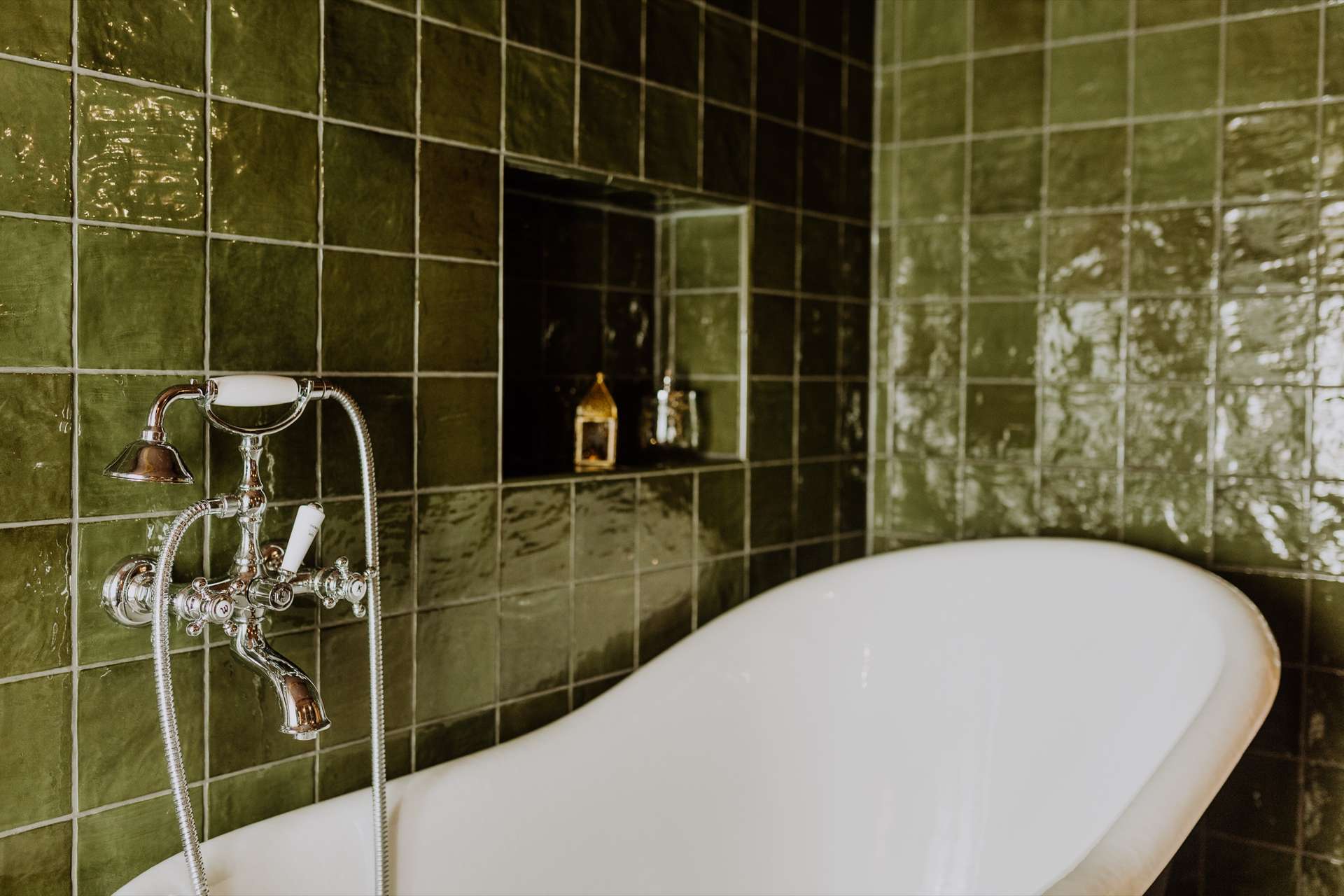 Freistehende weiße Badewanne mit verchromter Telefondusche vor glänzenden waldgrünen Fliesen