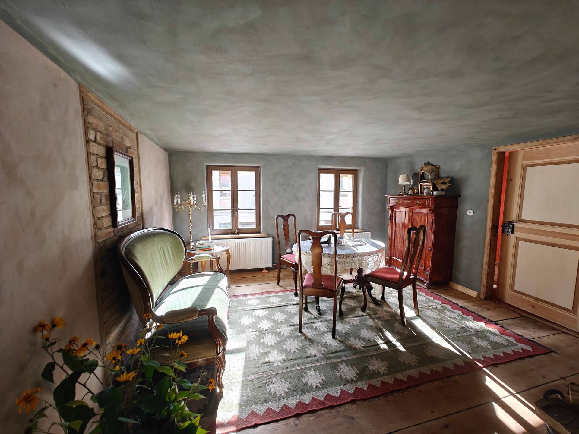 Lichtdurchfluteter historischer Saal der Alten Tischlerei mit Biedermeiersofa, Esstafel, Holzbalkendecke und Naturholzdielen