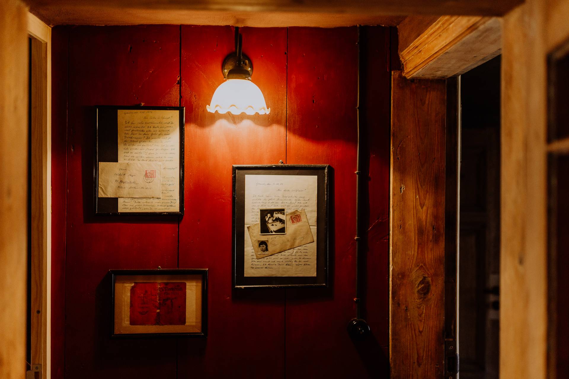 Eingangsbereich mit roter Holzvertäfelung, gerahmten historischen Dokumenten und gemütlicher Wandleuchte